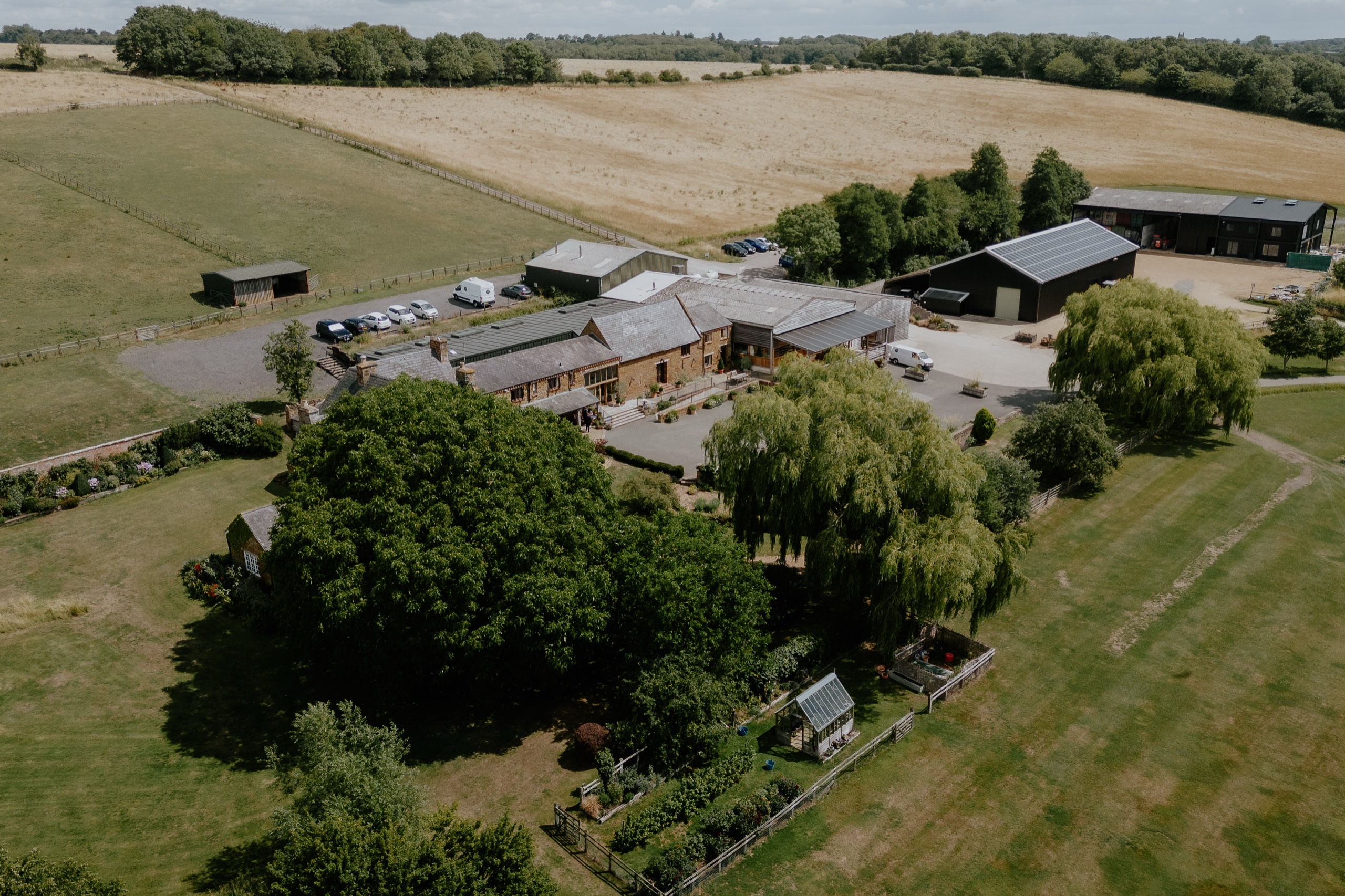 The farm from the air: the venue buildings, car park and farmhouse among lawns, willows and open fields, Crockwell Farm