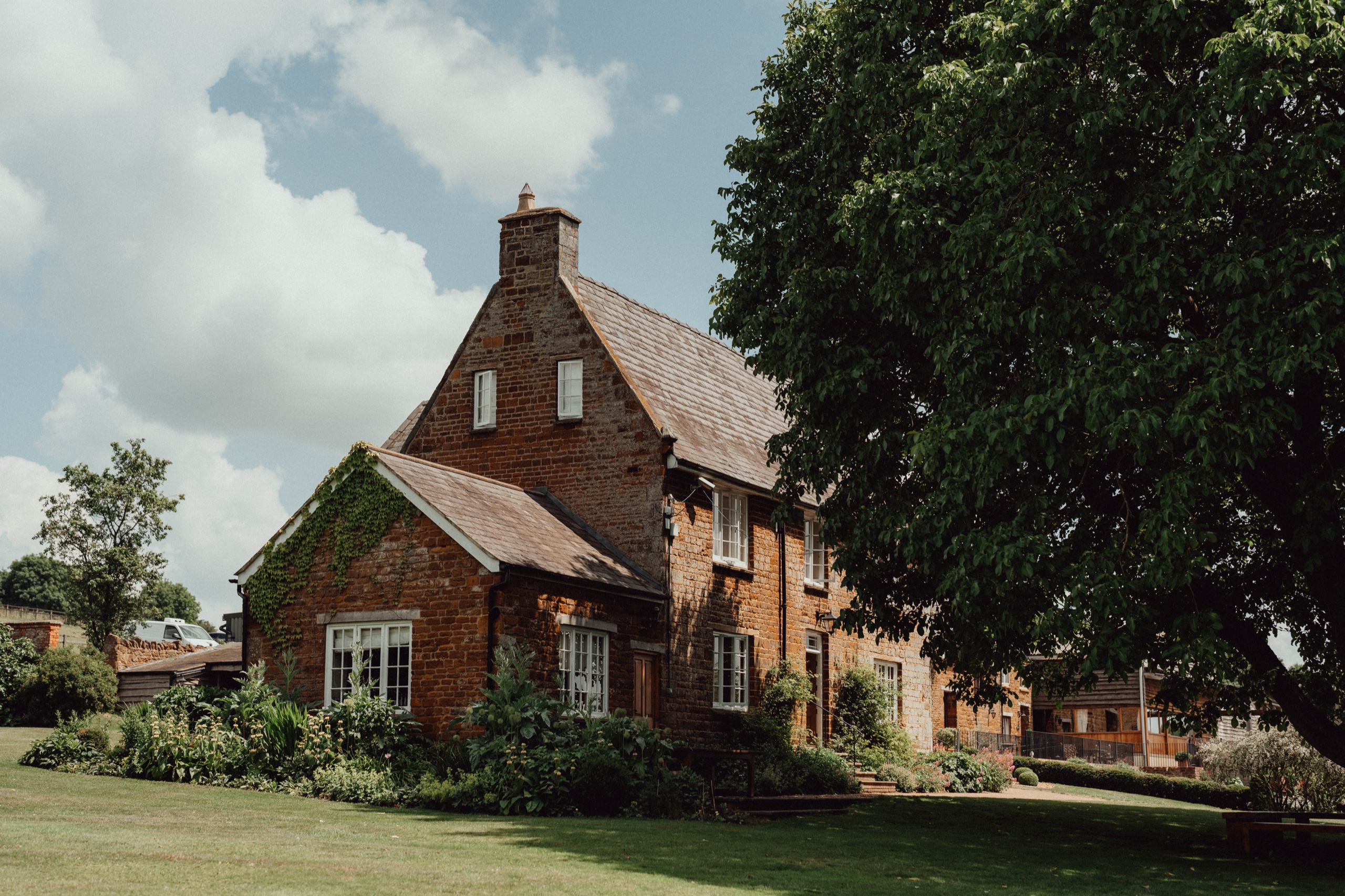 An ironstone house on the farm seen across the lawn, beside a large tree, Crockwell Farm