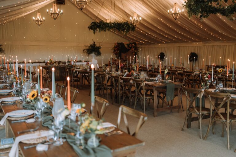 The starlit marquee laid with long rustic tables, cross-back chairs, chandeliers and hanging foliage, Crockwell Farm