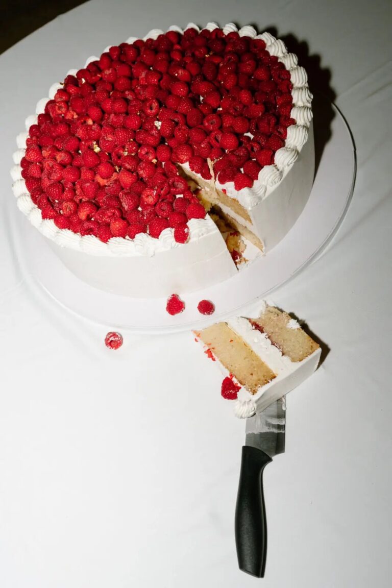A white cake topped with raspberries, cut at the reception, Cygnus Events