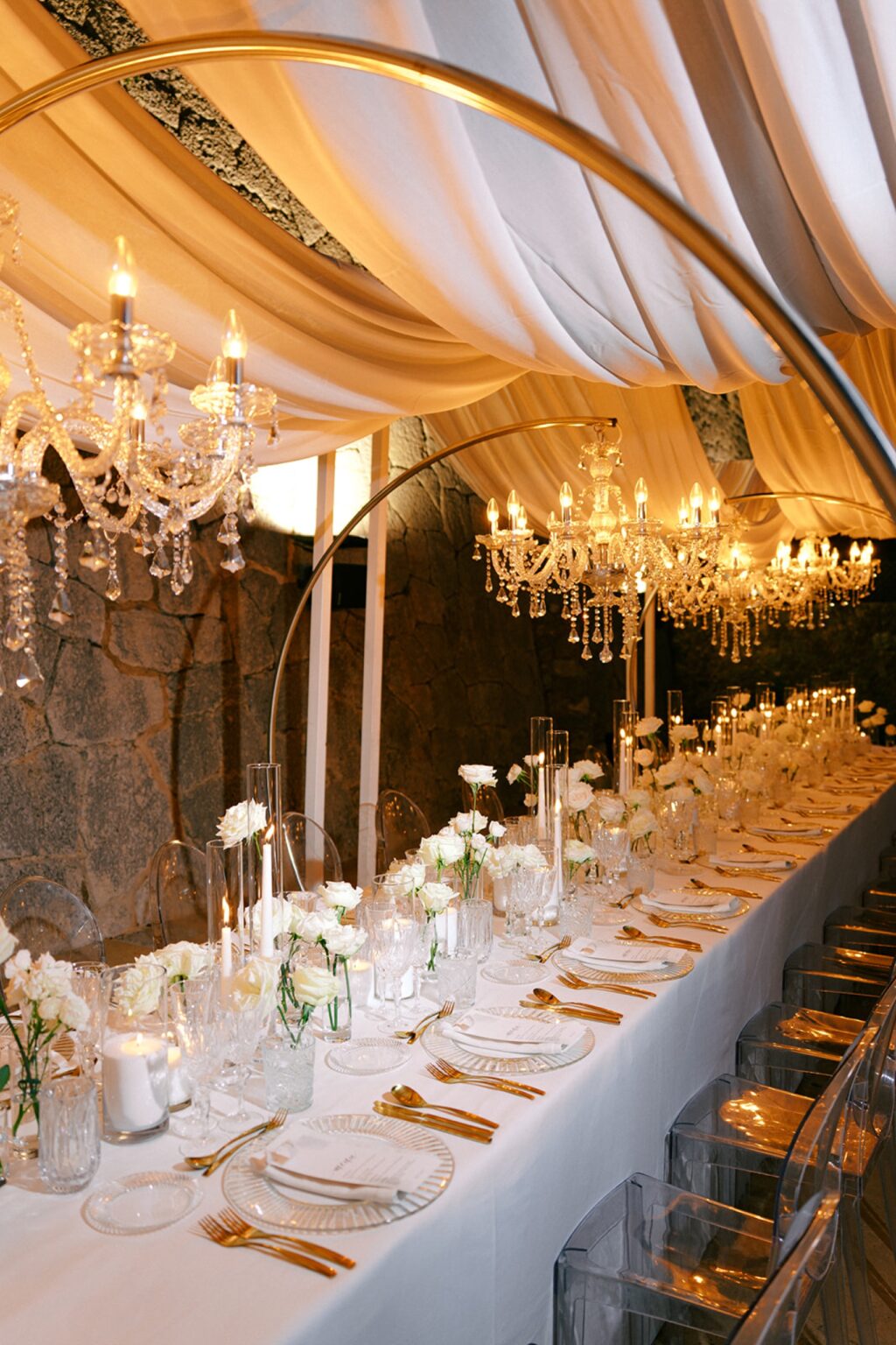 A candlelit dinner table under draped fabric and chandeliers