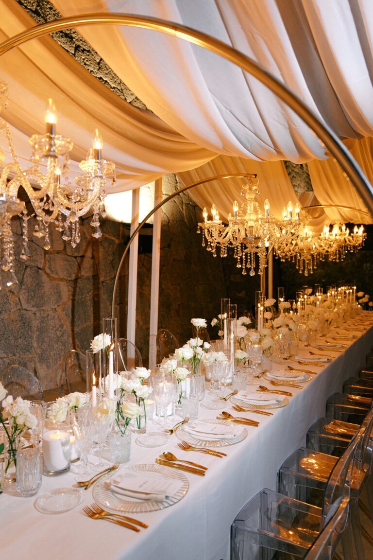 A candlelit dinner table under draped fabric and chandeliers, Cygnus Events