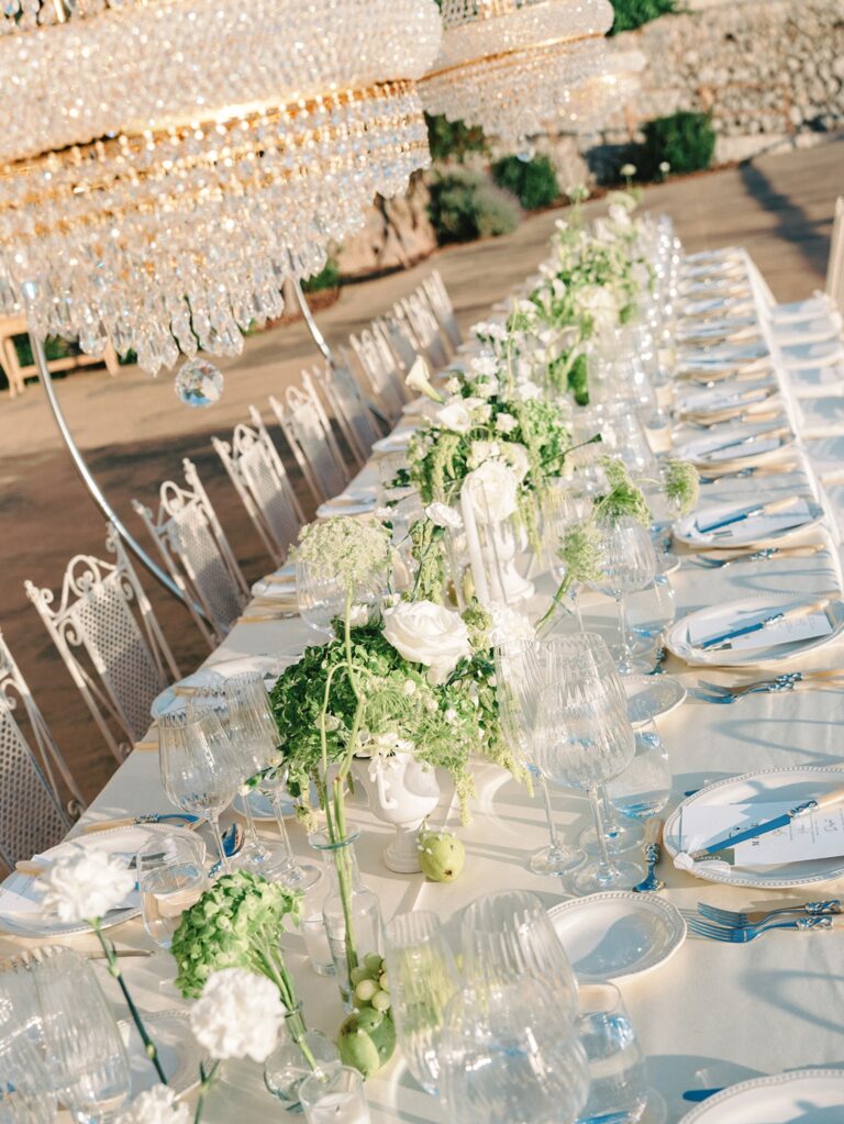 A banquet table with low greenery, glassware and crystal chandeliers, Cygnus Events