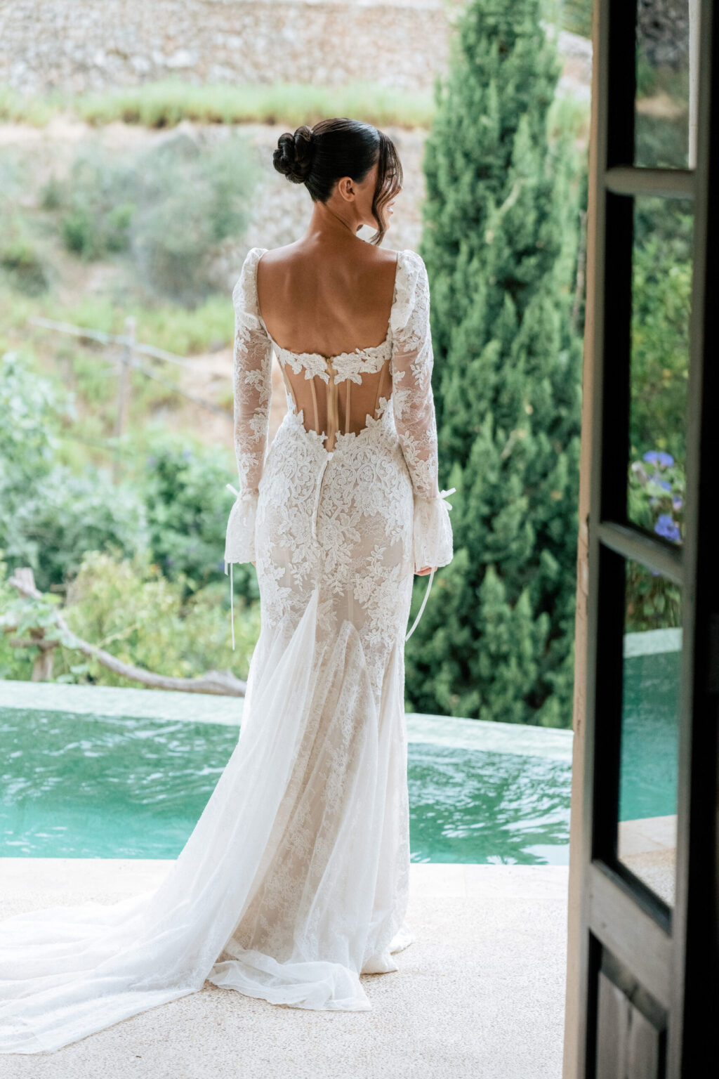 A bride in a lace gown on a terrace beside an infinity pool