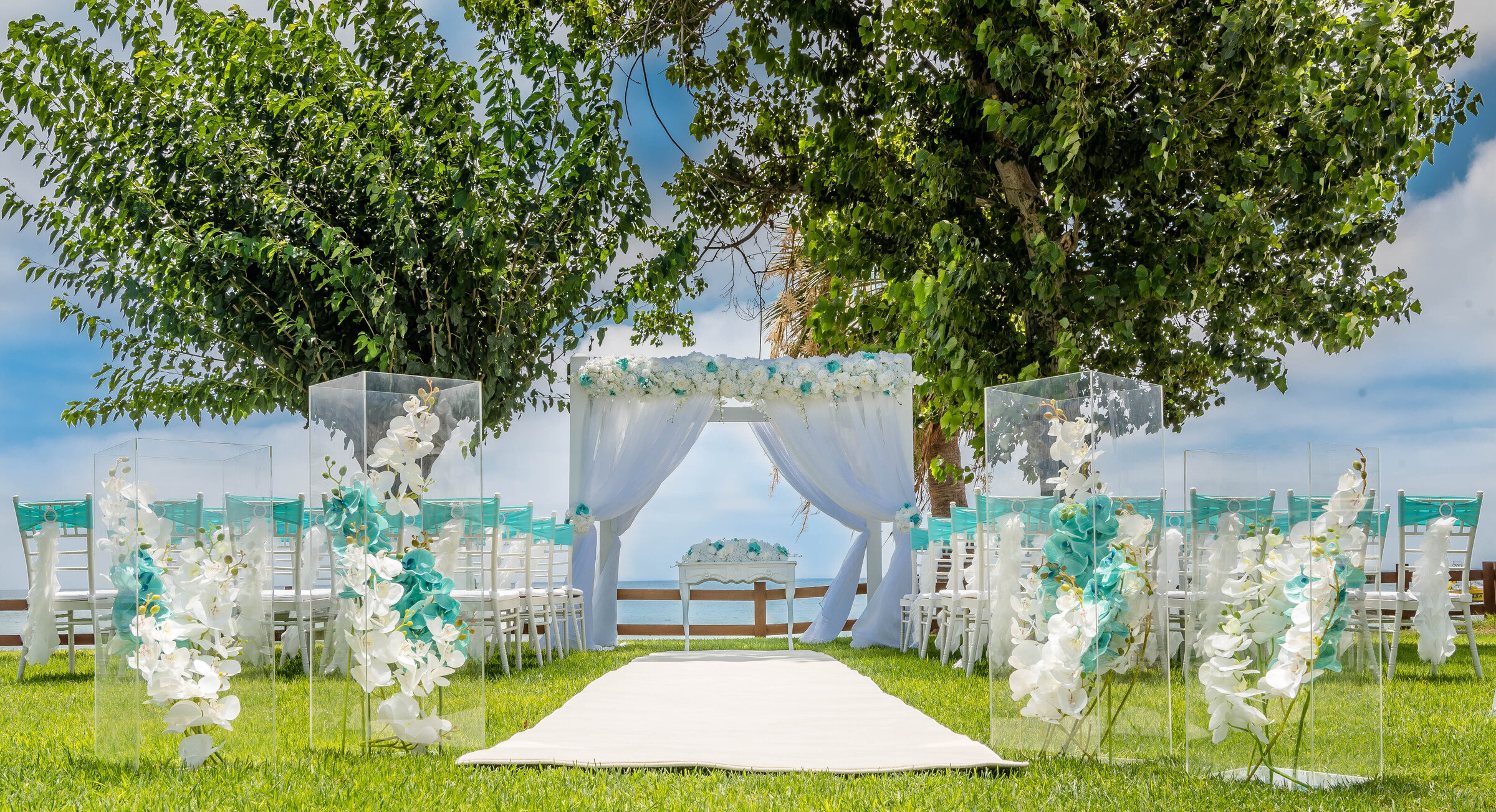 White aisle runner between clear floral columns on a seaside lawn, Cyprus Wedding Touches