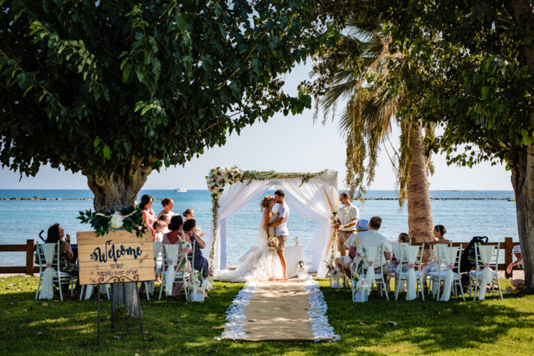 Beach blessing under a floral canopy with a welcome board and aisle, Cyprus Wedding Touches