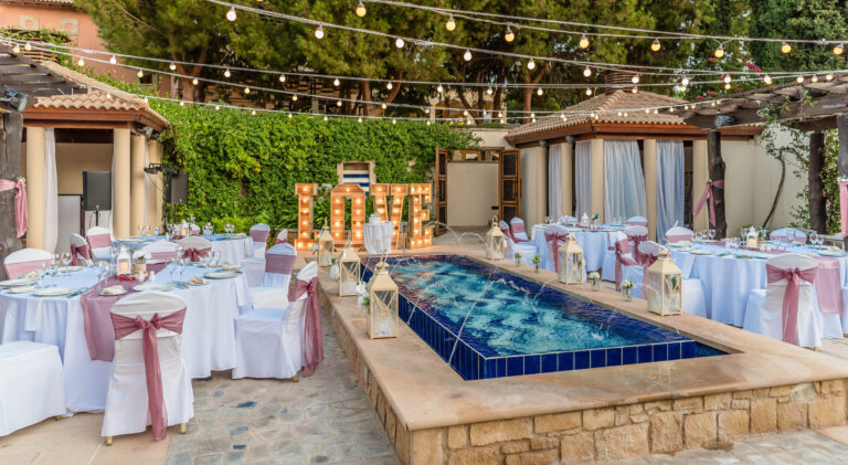 Courtyard reception tables with blush sashes and a lit LOVE sign beside a pool, Cyprus Wedding Touches