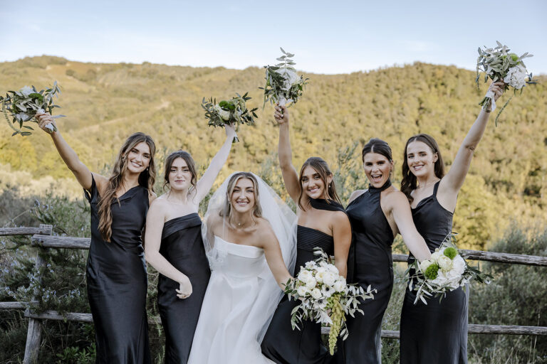 The bride and bridesmaids raising their bouquets above the Maremma hills, Daniele Vertelli Photography