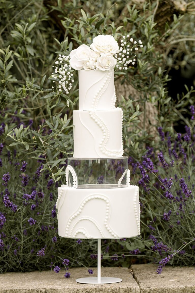 A white sculpted wedding cake with a sugar flower topper outdoors, Danielle's Cakes Pershore