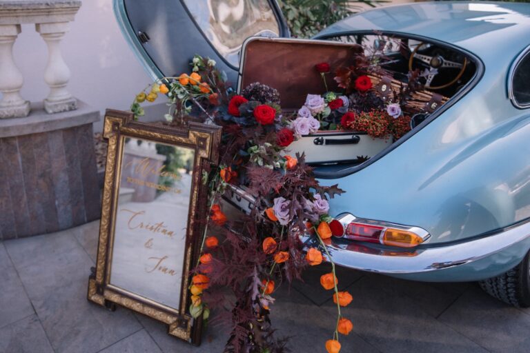 Vintage car boot overflowing with flowers beside a welcome sign, Daria Events and Weddings