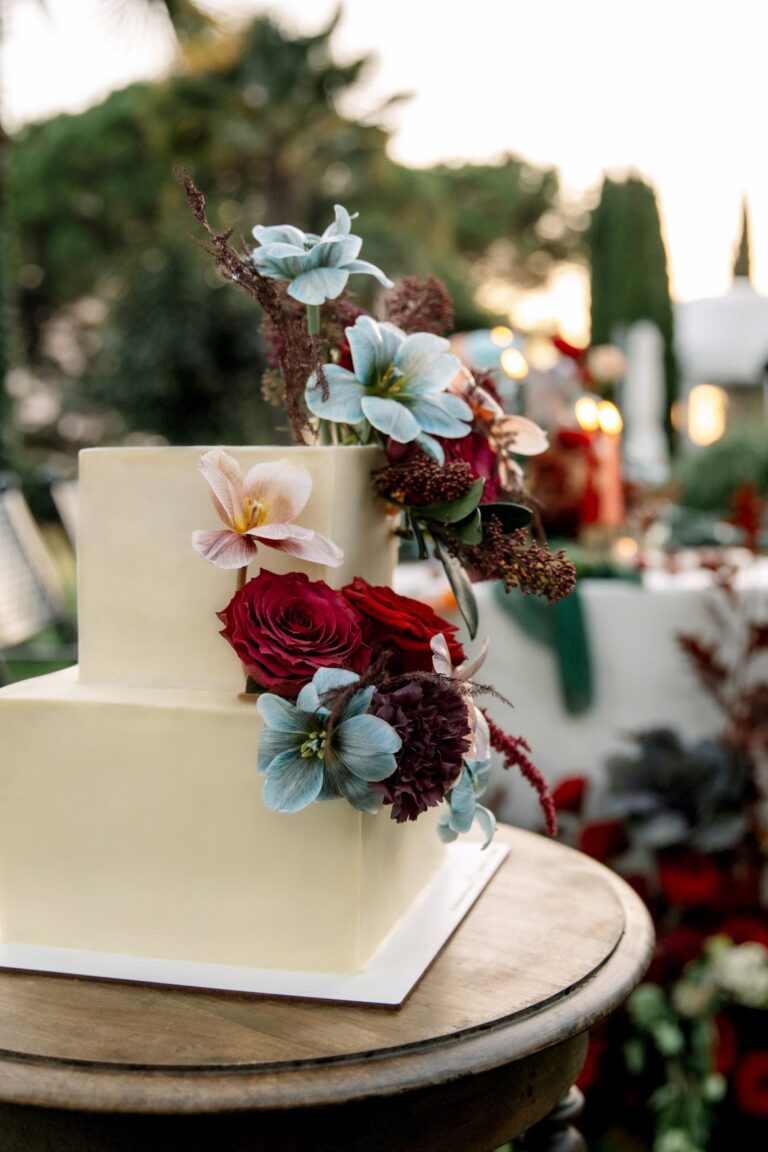 Wedding cake with blue and crimson flowers at golden hour, Daria Events and Weddings