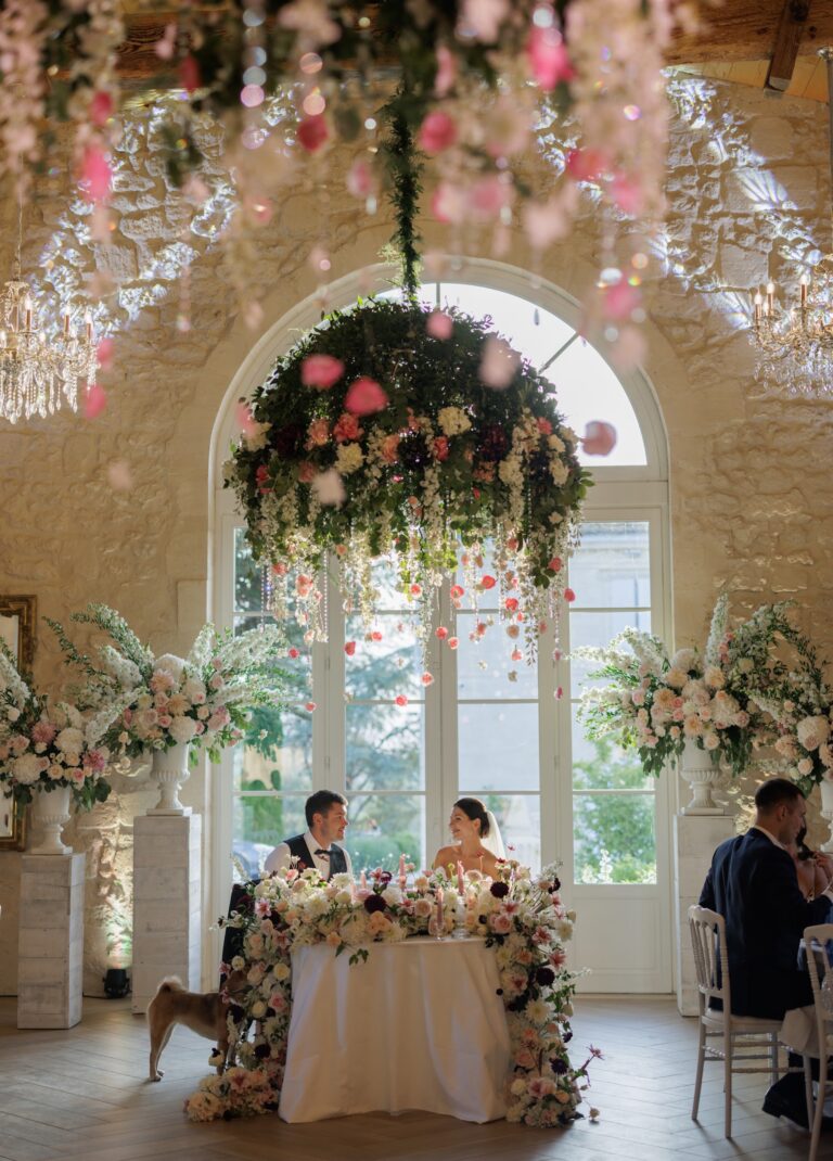 Couple at a floral-wreathed sweetheart table beneath a hanging flower chandelier, Daria Events and Weddings