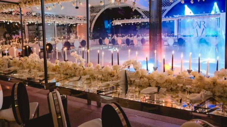 Mirrored long table with black tapers and white flowers facing the stage, monogram screen behind, Dario Varsalona