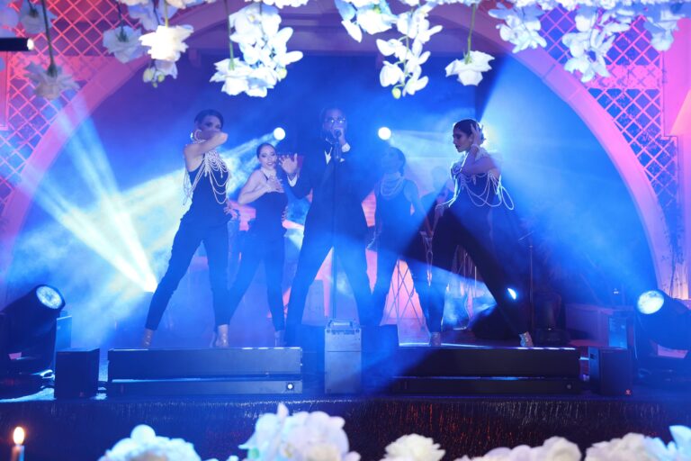 Live dancers on stage under hanging white orchids and blue stage lighting, Dario Varsalona