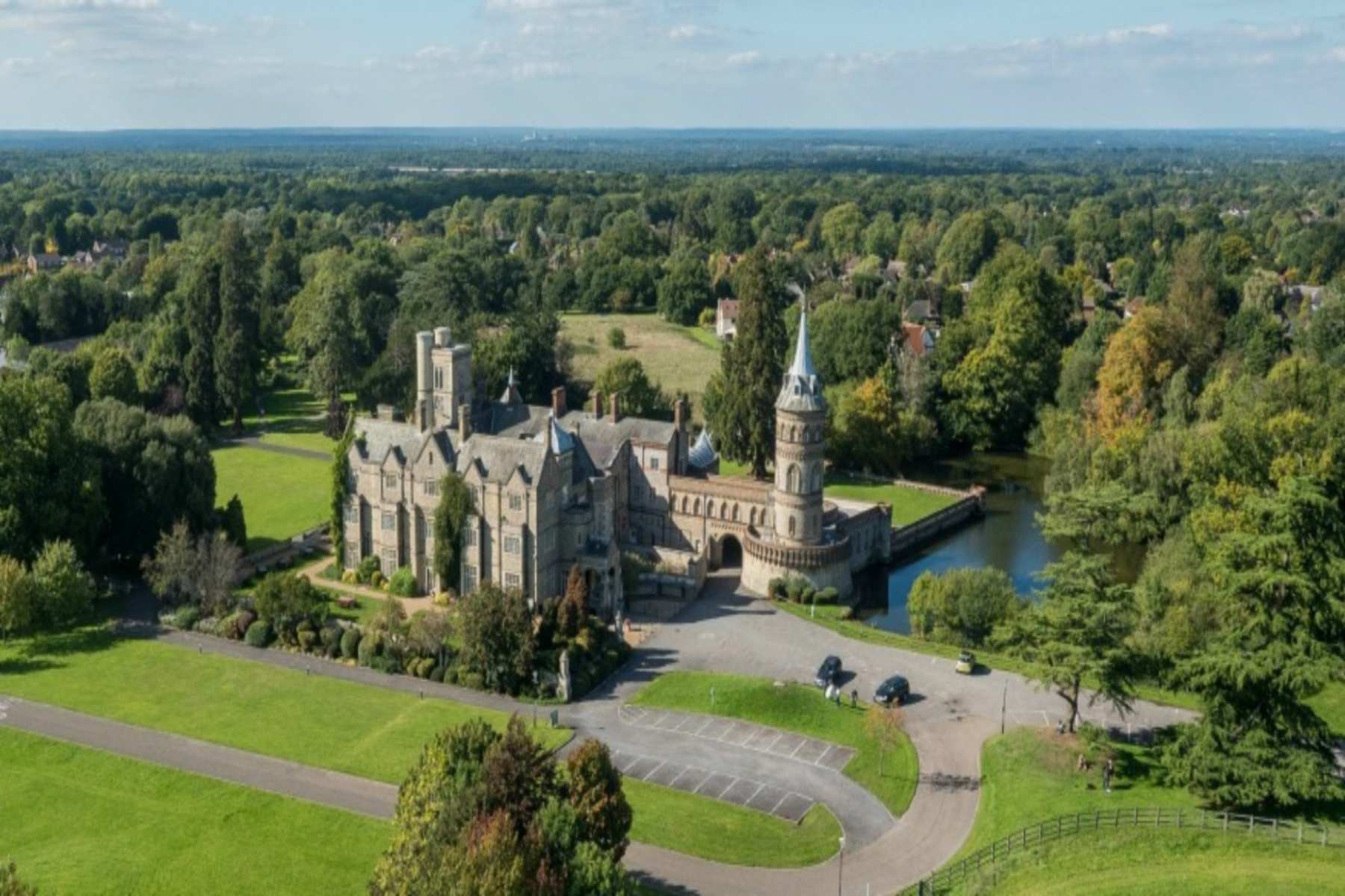 Aerial view of Horsley Towers, the lake and the drive, with Surrey woodland beyond, De Vere Horsley Estate