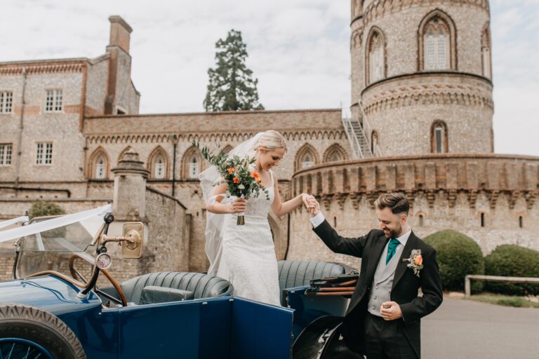 A bride stepping from a vintage car below the round tower, De Vere Horsley Estate
