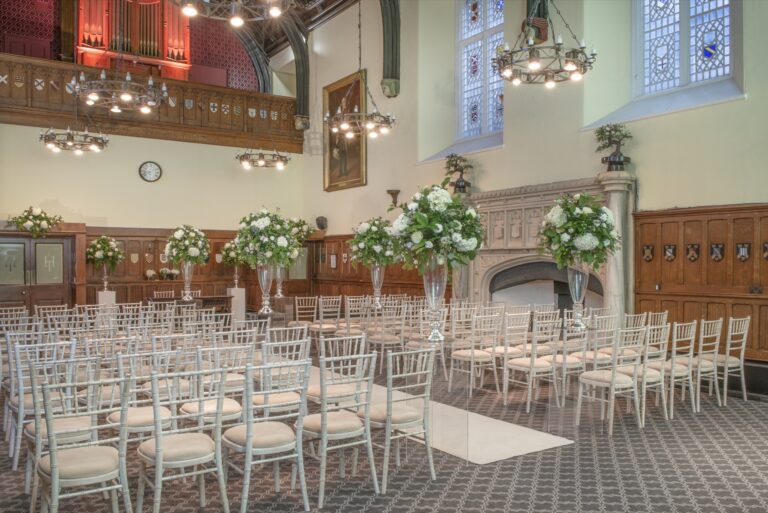 Ceremony chairs and white flower arrangements in the Great Hall beneath the stained glass, De Vere Horsley Estate