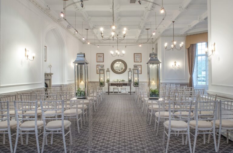A Towers function room with a coffered ceiling set for a ceremony with lanterns along the aisle, De Vere Horsley Estate
