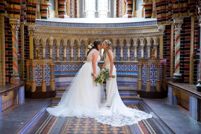 Two brides kissing in the tiled chapel in front of the carved altar screen, De Vere Horsley Estate