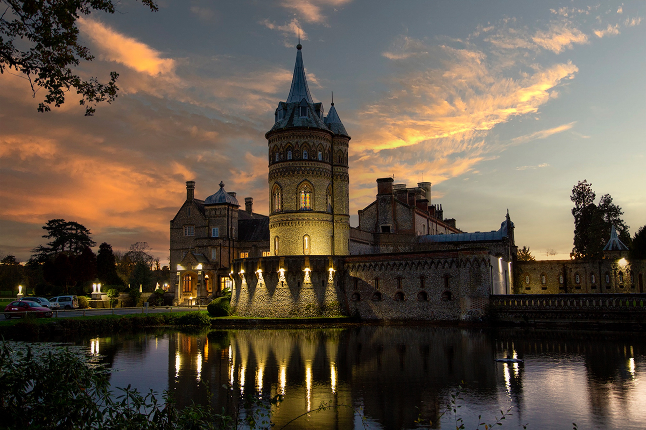 The mansion and Italian tower floodlit at sunset above the lake, De Vere Horsley Estate