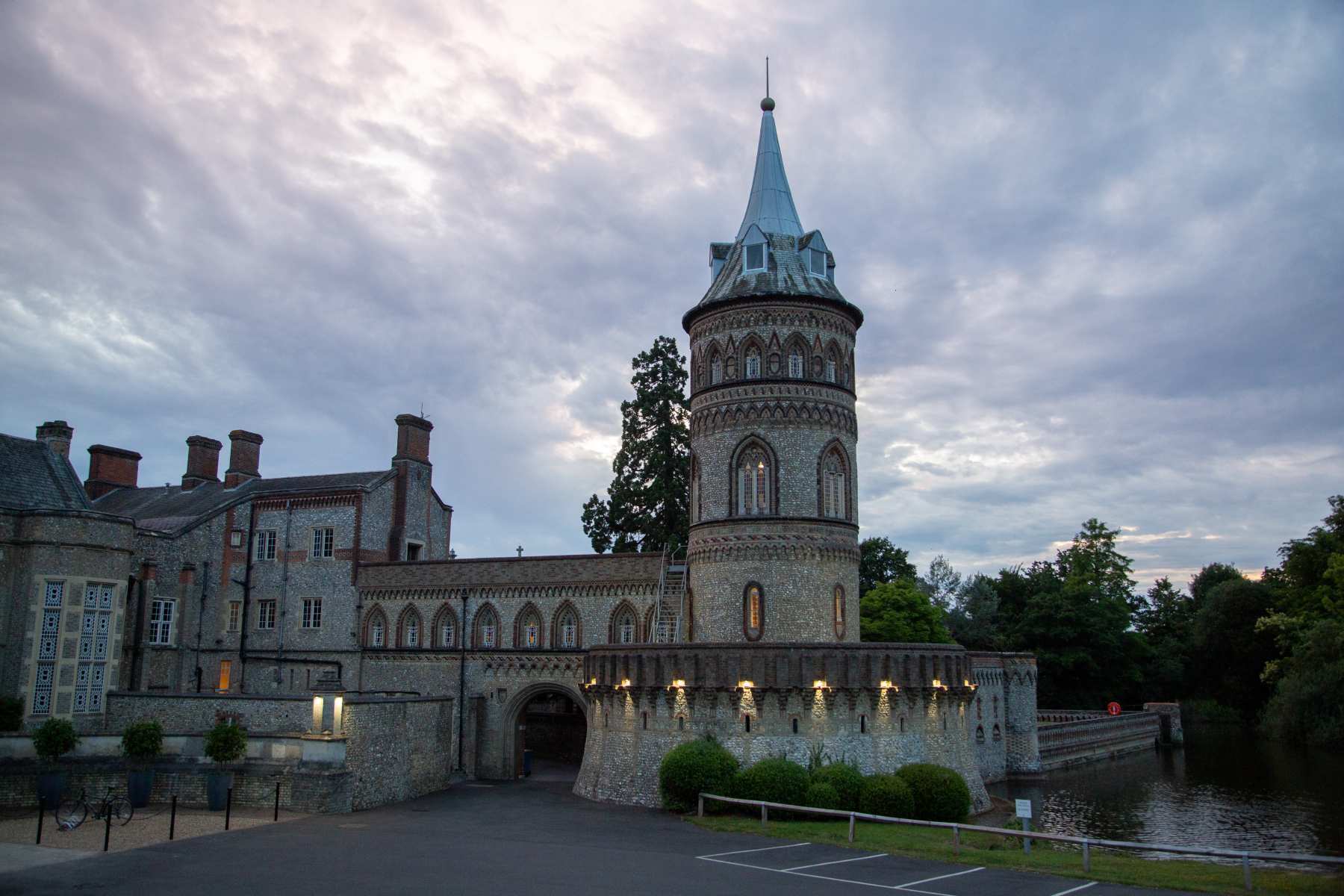 The Italian tower and battlemented gateway beside the lake under a cloudy sky, De Vere Horsley Estate