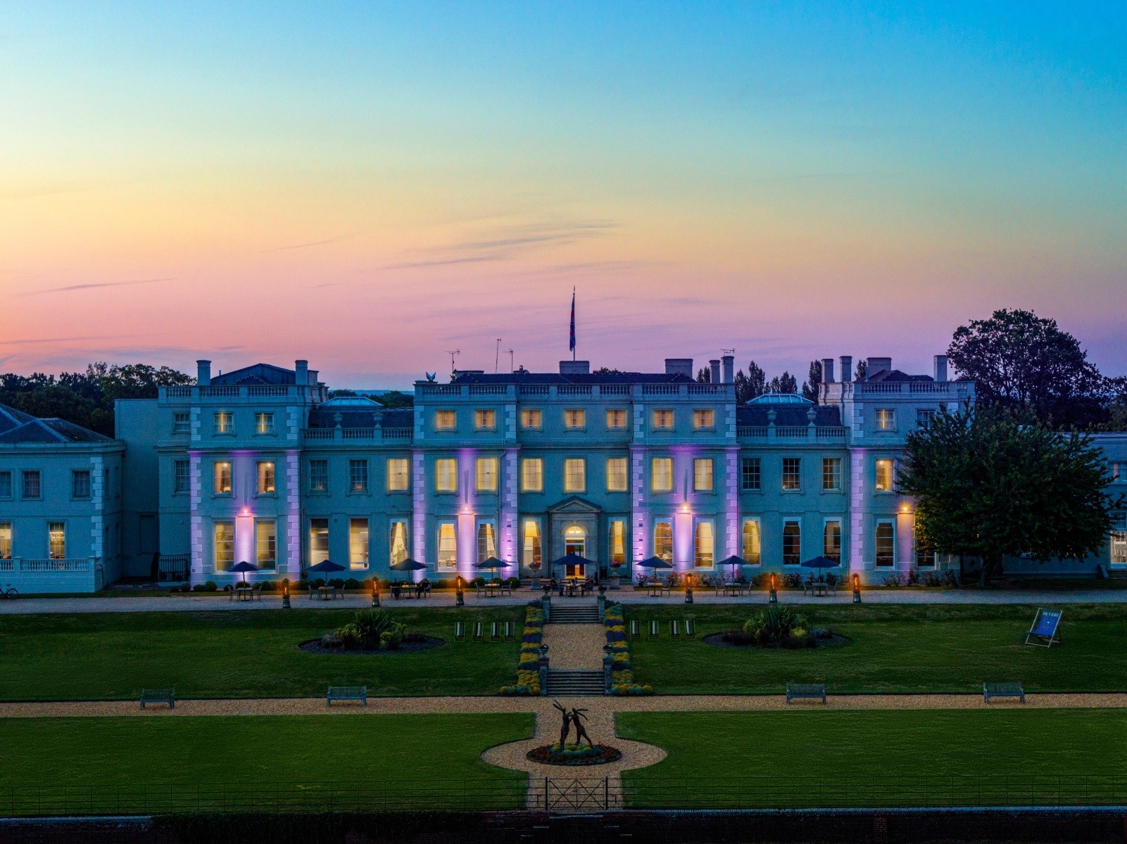 The mansion house lit at dusk above the lawn, De Vere Wokefield Estate