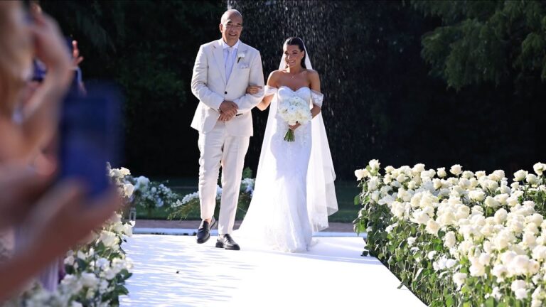 A bride is walked down a rose-lined aisle at Finca La Concepción, Marbella, at L and D's wedding (still from their film), Denee Motion