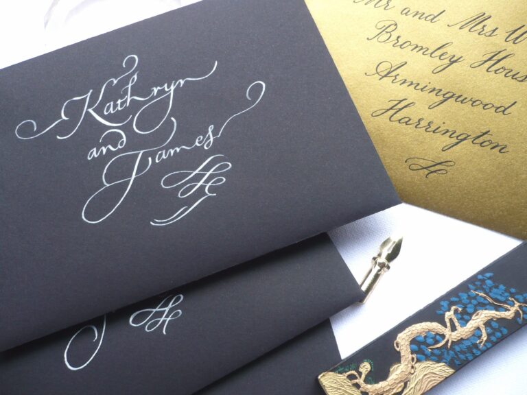 White ink calligraphy names on dark envelopes beside a gold envelope, Denise Hagon Calligrapher