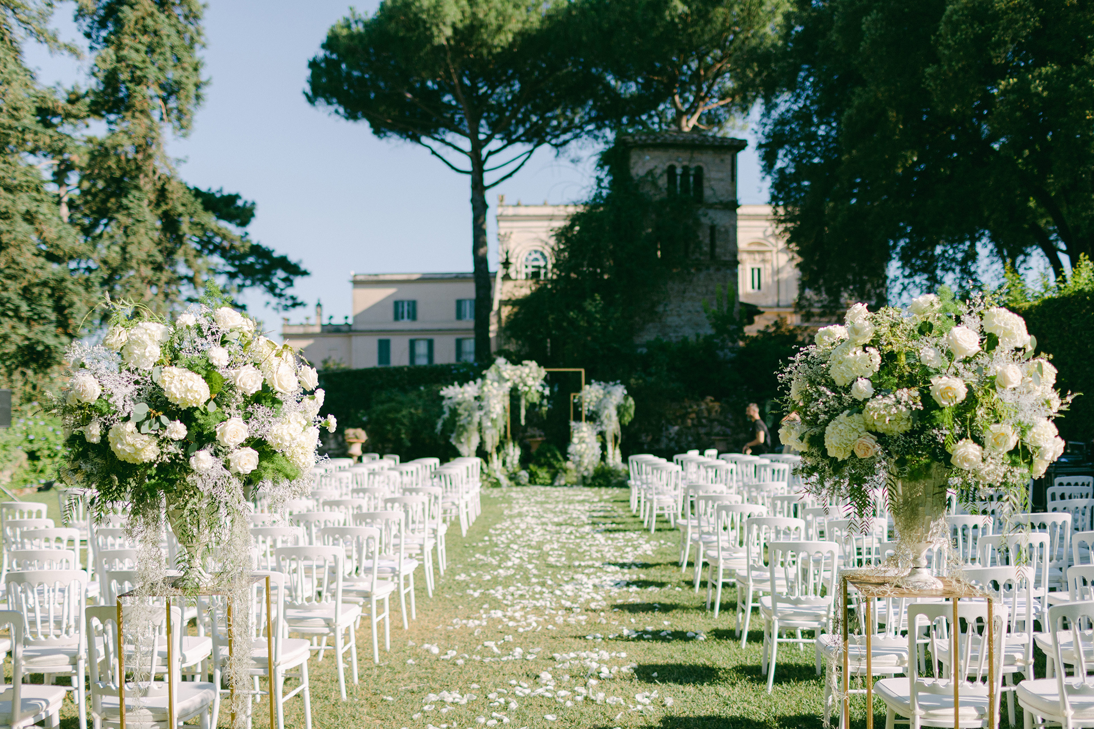 Ceremony aisle on the lawn at Villa Aurelia, Rome: white chairs, petals and urns of white flowers under umbrella pines, Denise More
