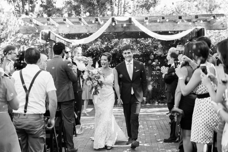 The couple walking back up the aisle through cheering guests, in black and white, Despina Craig Events