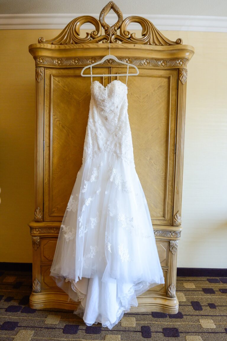 A lace wedding gown hanging from an ornate wardrobe, Despina Craig Events