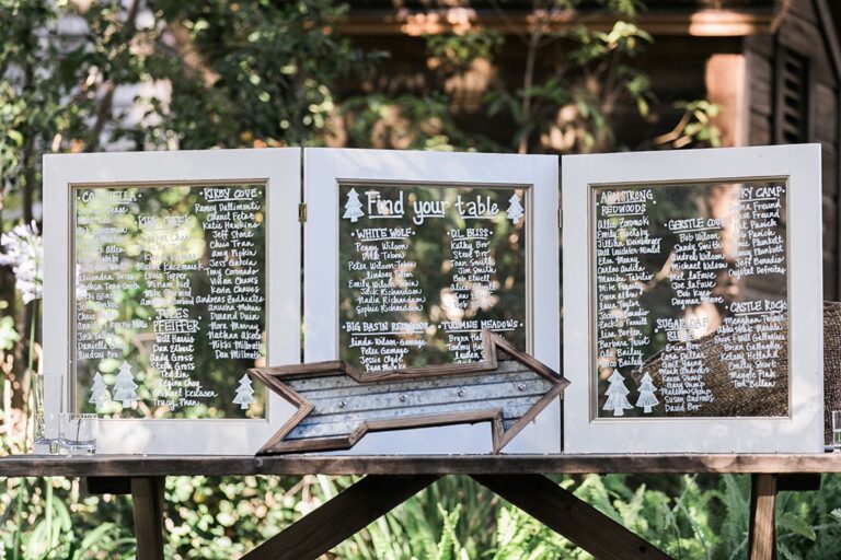 Hand-lettered seating charts in white frames with a carved wooden arrow, Despina Craig Events
