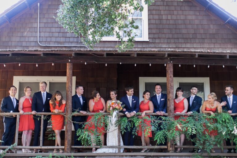 Wedding party lined up along a timber porch hung with greenery, bridesmaids in coral, Despina Craig Events