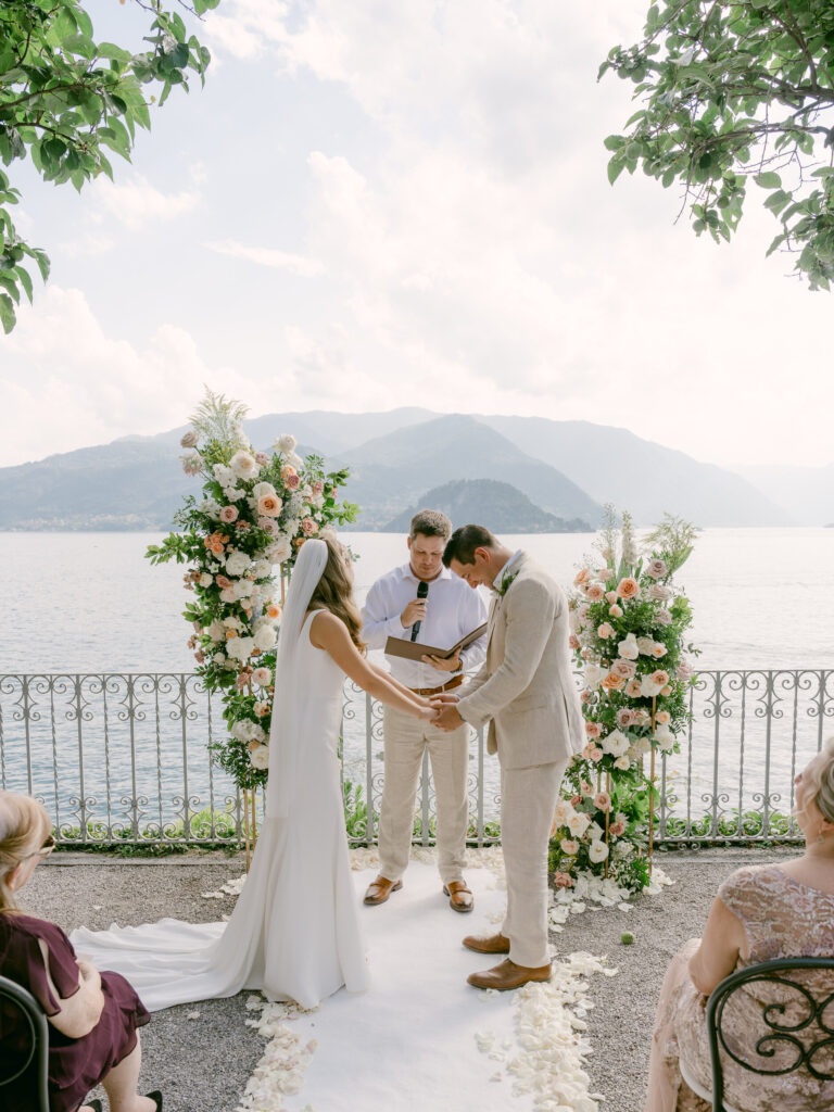Vows under a floral arch with the lake and mountains behind. Brooke and Austin's wedding at Villa Cipressi, Lake Como, Detito Photography