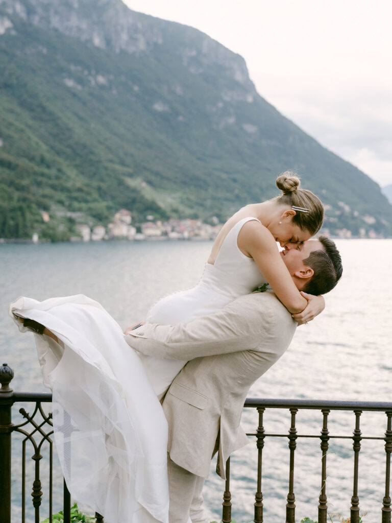The groom lifting the bride at the railing above the lake. Brooke and Austin's wedding at Villa Cipressi, Lake Como, Detito Photography