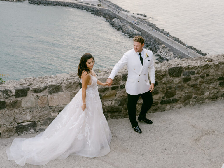 Bride and groom on the castle walls with the causeway and sea below. Erica and Dustin's wedding at the Aragonese Castle, Ischia, Detito Photography