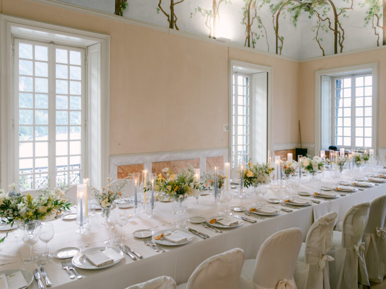A long dinner table laid with flowers and candles in a tall-windowed room. Brooke and Austin's wedding at Villa Cipressi, Lake Como, Detito Photography