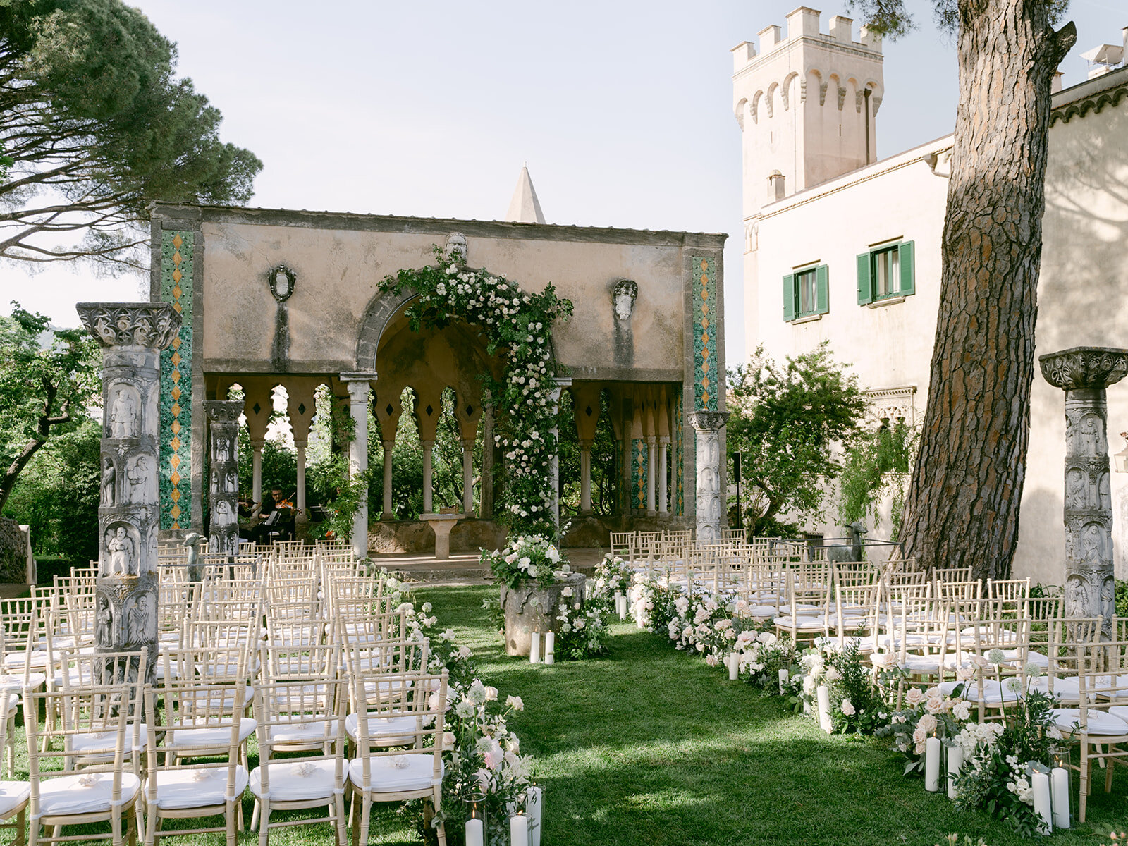 Rows of chairs and white roses laid out for the ceremony in the garden, the villa tower behind. Alex and Andrew's wedding at Villa Cimbrone, Ravello, Amalfi Coast, Detito Photography