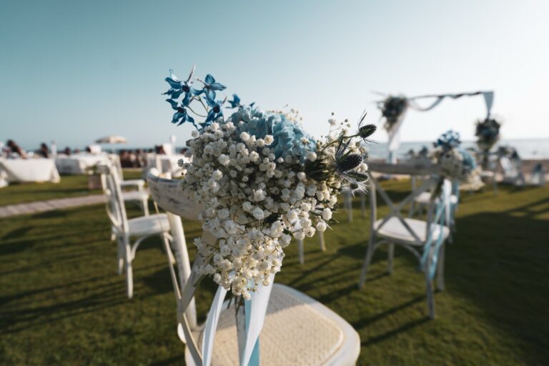 A seaside ceremony set-up on a lawn: white chairs dressed with gypsophila and blue delphinium, the arch facing the sea, Diamante Your Wedding in Italy