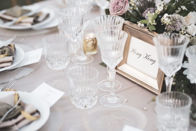 Place settings with crystal glasses and a framed table name card among pale flowers, Diamante Your Wedding in Italy
