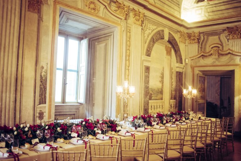A long winter wedding table with red poinsettias and candelabra in a frescoed salon, Diamante Your Wedding in Italy