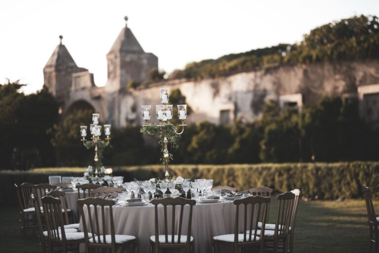 Tables with gilded candelabra and greenery in the castle gardens, the old gate towers behind, Diamante Your Wedding in Italy