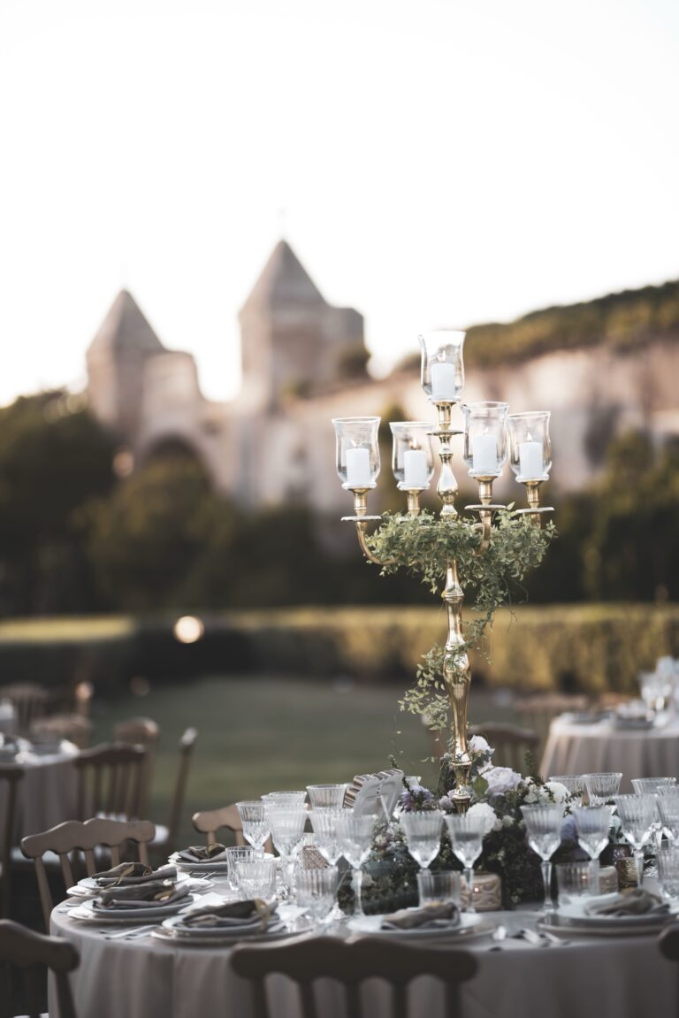 A gold candelabra wound with greenery above a laid table, the castle gate towers softly behind, Diamante Your Wedding in Italy