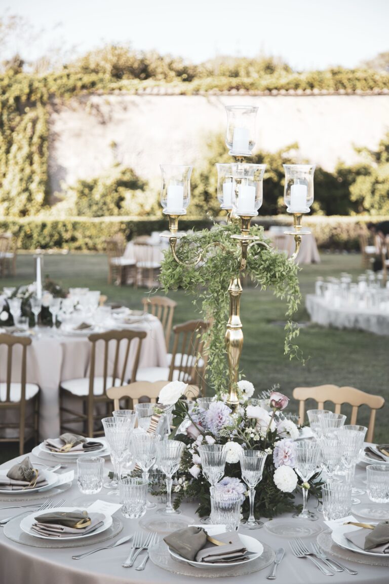 A round garden table with a tall candelabra, white and lilac flowers and gold chairs, Diamante Your Wedding in Italy
