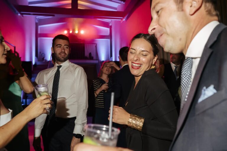 Guests laughing together at the reception, lit in red and blue, Diego Giusti Photographer