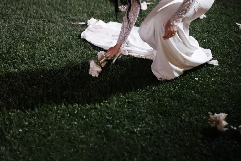 The bride kneeling in the grass at night, reaching for a fallen flower, Diego Giusti Photographer