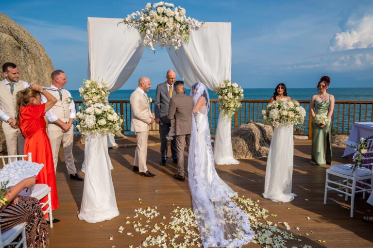 The bride walks the petal-strewn aisle to a white floral arch above the sea, Dimas Frolov Photography