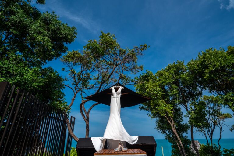 A wedding dress hung beneath an umbrella with the sea beyond, Dimas Frolov Photography
