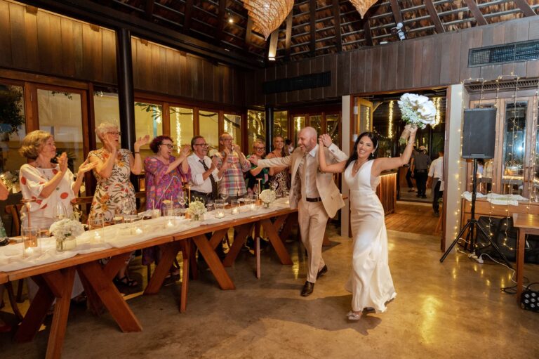 The bride arrives at the wedding dinner with her bouquet raised, guests cheering, Dimas Frolov Photography