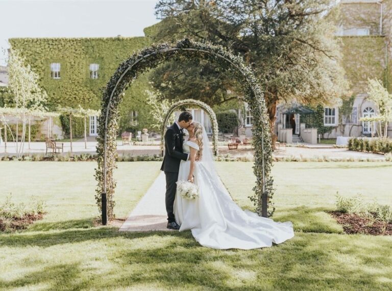 A couple beneath a rose arch in the gardens, Down Hall Country House Hotel